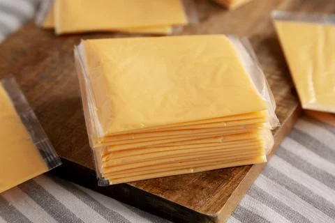 Wrapped Yellow Cheddar Cheese in a Stack on a wooden board, side view. Clos.. Stock Photos