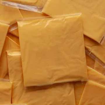 Wrapped Yellow Cheddar Cheese in a Stack on a wooden board, top view. Stock Photos