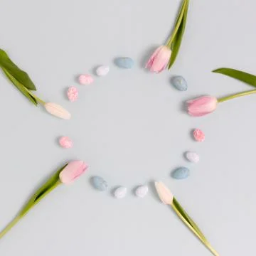 Wreath made of colorful easter eggs and flowers on a blue pastel background. Stock Photos