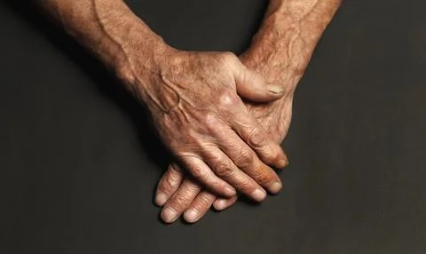 Wrinkled hands of an elderly man on a table close-up on a black Stock Photos