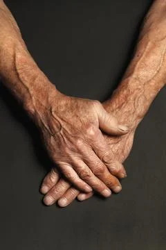Wrinkled hands of an elderly man on a table close-up on a black Stock Photos