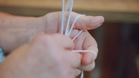 Wrinkled hands expertly loop yarn around needles. Serene elderly grandmother 動画素材 334792333
