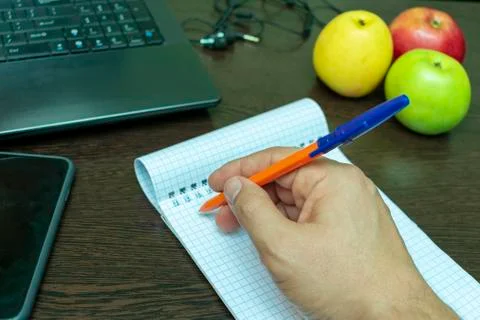 Write ideas into a notebook with a pen, laptop, headphones and apples for hea Stock Photos