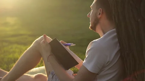 A writer or poet writes a work under a tree on a sunny evening at sunset Stock Footage 89182710