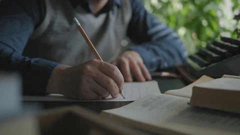 Writer is working on a draft, writes in pencil. Typewriter on the desk Stock Footage 116673993