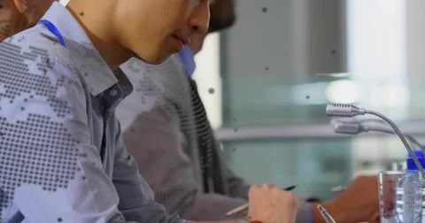 Writing Asian man in patterned shirt and blue lanyard at meeting table with Stock Photos