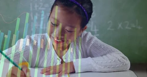 Writing Chinese student solving math problems at desk in class, with chalkboard Stock Photos