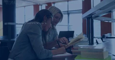 Writing denim student and patterned-top tutor leaning in library using notebook Stock Photos