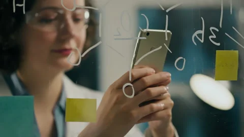 Writing formulas female scientist keeps looking at the screen of modern smar Stock Footage 249842817