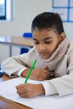 Writing in lined notebook at school desk, female youth wearing knitted scarf Stock Photos