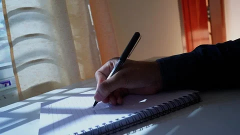 Writing in a Notebook by Sunlit Window, A person writing in a notebook on a.. Stock Footage 317736596