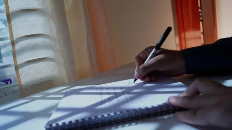 Writing in a Notebook by Sunlit Window, A person writing in a notebook on a.. Stock Footage 317736603
