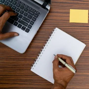 Writing on a notepad and typing on a keyboard while working on a project. A l Stock Photos