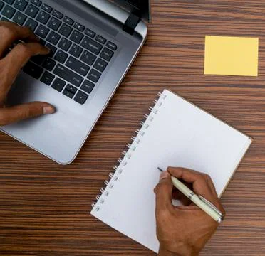 Writing on a notepad and typing on a keyboard while working on a project. A l Stock Photos