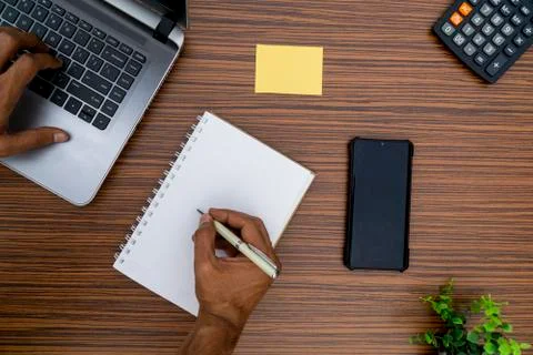 Writing on a notepad and typing on a keyboard while working on a project. A l Stock Photos