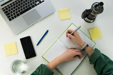 Writing in notepad sitting at desk with smarphone and laptop computer Stock Photos