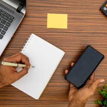 Writing on a notepad while holding a mobile phone working in an office enviro Stock Photos
