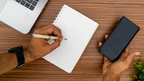 Writing on a notepad while holding a mobile phone working in an office enviro Stock Photos