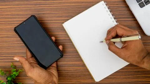 Writing on a notepad while holding a mobile phone working in an office enviro Stock Photos