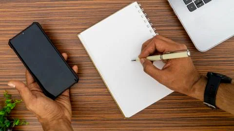 Writing on a notepad while holding a mobile phone working in an office enviro Stock Photos