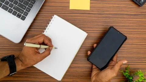 Writing on a notepad while holding a mobile phone working in an office enviro Stock Photos