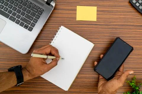 Writing on a notepad while holding a mobile phone working in an office enviro Stock Photos