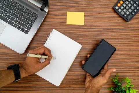 Writing on a notepad while holding a mobile phone working in an office enviro Stock Photos