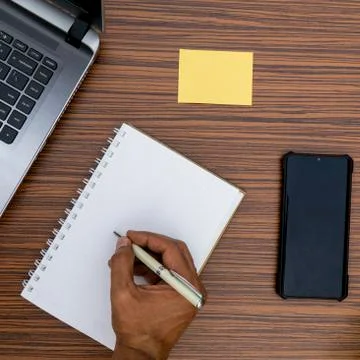 Writing on a notepad while working from home. A lap top, a mobile, calculator Stock Photos