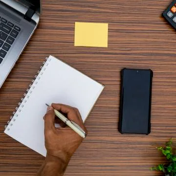 Writing on a notepad while working from home. A lap top, a mobile, calculator Stock Photos