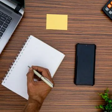 Writing on a notepad while working from home. A lap top, a mobile, calculator Stock Photos