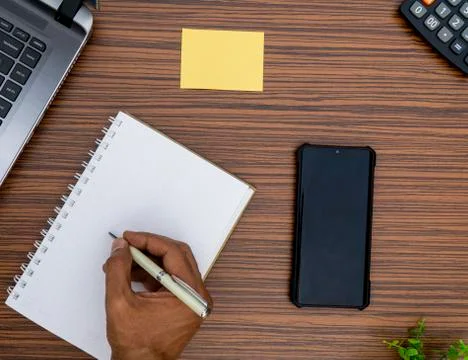Writing on a notepad while working from home. A lap top, a mobile, calculator Stock Photos