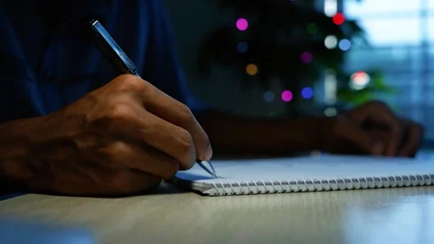 Writing notes beside holiday lights, Close-up of a person writing in a spir.. 動画素材 346484158