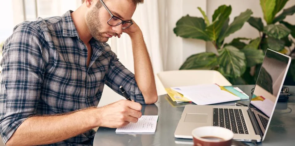 Writing notes down infront of laptop at home Stock Photos