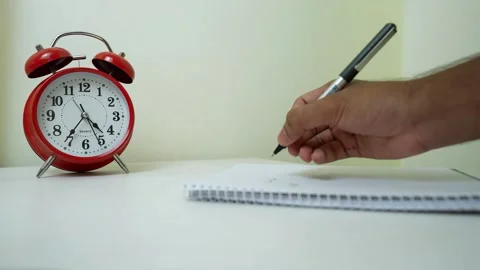 Writing Notes with Red Alarm Clock, Hand writing on a notepad next to a red.. Stock Footage 317737468