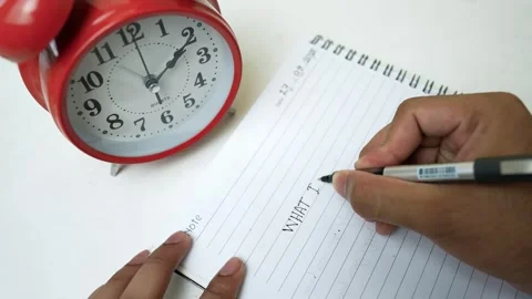 Writing Notes with Red Alarm Clock, Person writing in a notebook with a red.. Stock Footage 318057186