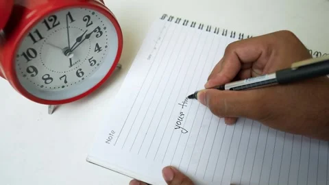 Writing Notes with Red Alarm Clock, Person writing in a notebook with a red.. Stock Footage 318057193