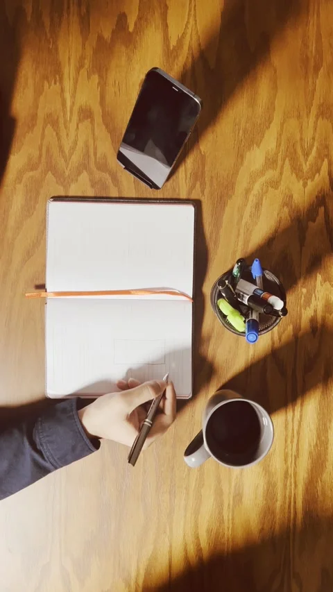 Writing in an open notebook at a wooden desk, top-down view Stock Footage 345150636