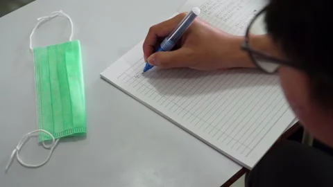 Writing on a paper of white notebook with a face mask on the table. School, l Stock Footage 167811809