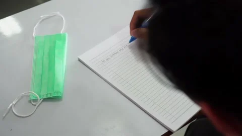 Writing on a paper of white notebook with a face mask on the table. School, l Stock Footage 167811811