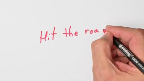 Writing with a red marker the sentence: Hit the road Stock Footage 221782058