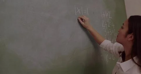 Writing teacher solving absolute value equation on green chalkboard holding Stock Photos