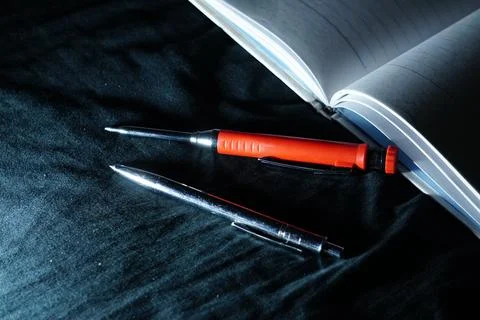 Writing tools rest on a notebook under a sharp, cool blue light, creating a focu Stock Photos