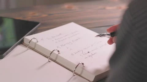 Writing a weekly plan and schedule in a notebook on a desk for business Stock Footage 343927486