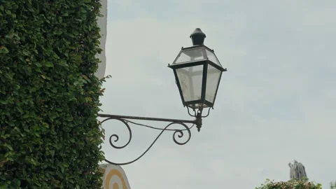 Wrought Iron Wall Lantern on a Scrolled Bracket Against a Pale Sky Video stock 342330757