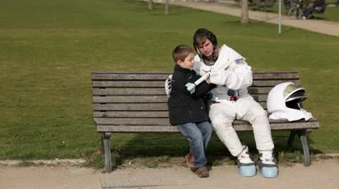WS, Lockdown of an astronaut and a young boy sitting on a park bench playing Stock Footage 10700819