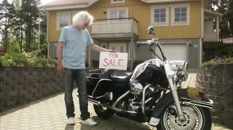 WS Portrait of senior man holding For Sale sign at Harley Davidson, suburban Stock Footage