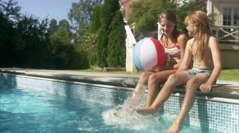 WS Two sisters sitting at edge of swimming pool splashing water with feet Video stock 11343479