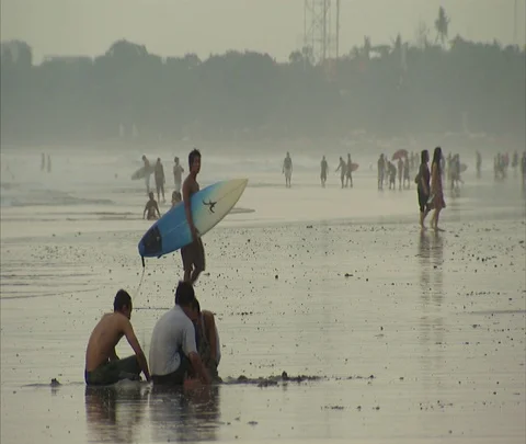 WS young man with surfboard walks past beachgoers in wet sand Stock Footage 86747255