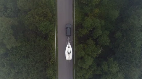 Yachting boat on trailer pulled by car on winding mountain road - drone aerial Stock Footage 99413592