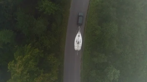 Yachting boat on trailer pulled by car on winding mountain road - drone aerial Stock Footage 99583370